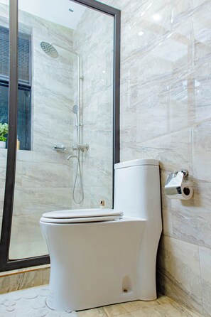 Un baño moderno con ducha envuelta en vidrio, inodoro y dispensador de papel higiénico adherido a la pared.