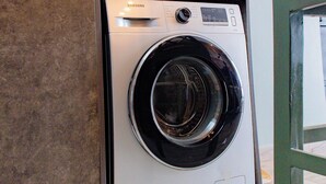 A modern laundry room with a Samsung washing machine, wooden cabinets, and a wall-mounted drying rack. - Rustic, quiet and cozy 1-bedroom condo with fantastic views. (Kampala)