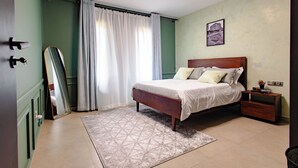 A bedroom with a bed, a nightstand, a mirror, a window with curtains, and a wall-mounted picture. - Rustic, quiet and cozy 1-bedroom condo with fantastic views. (Kampala)