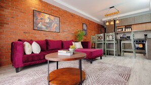 A living room with a brick wall, a sofa, a coffee table, and a kitchen area with a microwave and stove. - Rustic, quiet and cozy 1-bedroom condo with fantastic views. (Kampala)