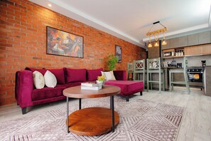 Ein Wohnzimmer mit Backsteinwand, einer Couch, einem Couchtisch und einer Küchenzeile inklusive Mikrowelle und Herd.