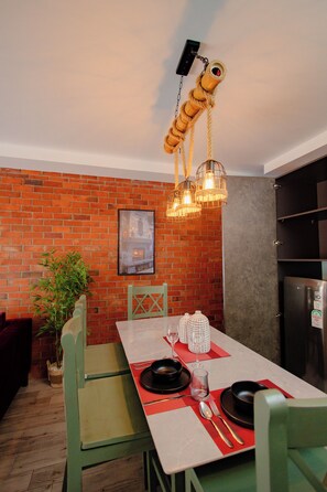 Un rincón comedor con pared de ladrillo, una mesa dispuesta para dos personas y una lámpara colgante.