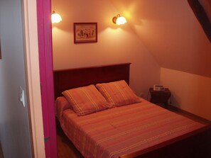 A bedroom with a bed, a nightstand, a lamp, and a wall-mounted picture. - Gite 6/8 persons PAIMPOL BRETAGNE (Paimpol)