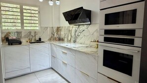 Una cocina moderna con armarios blancos, encimera de mármol y hornos empotrados.