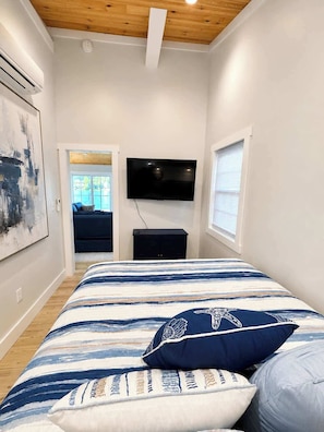 Quarto com cama, televisão na parede e janela.