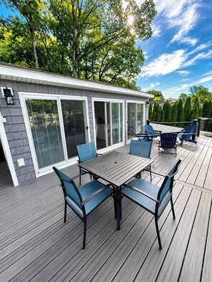 Um terraço com mesa e cadeiras, uma área de varanda coberta e uma casa com portas de correr de vidro.