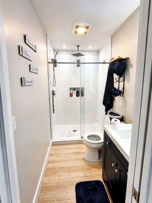 Uma casa de banho moderna com cabine de duche em vidro, sanita e toucador com suporte para toalhas.