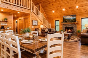 A wooden interior with a dining area, a fireplace, and a staircase. - Cozy 3BR Cabin w/ Hot Tub, Pool Table & Arcade (Sevierville)