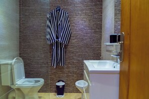 Une salle de bain avec un peignoir rayé accroché, des toilettes, un bidet et un lavabo.