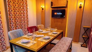 Een eetruimte met een lange tafel gedekt voor vier personen, een bank en een aan de muur bevestigde televisie.
