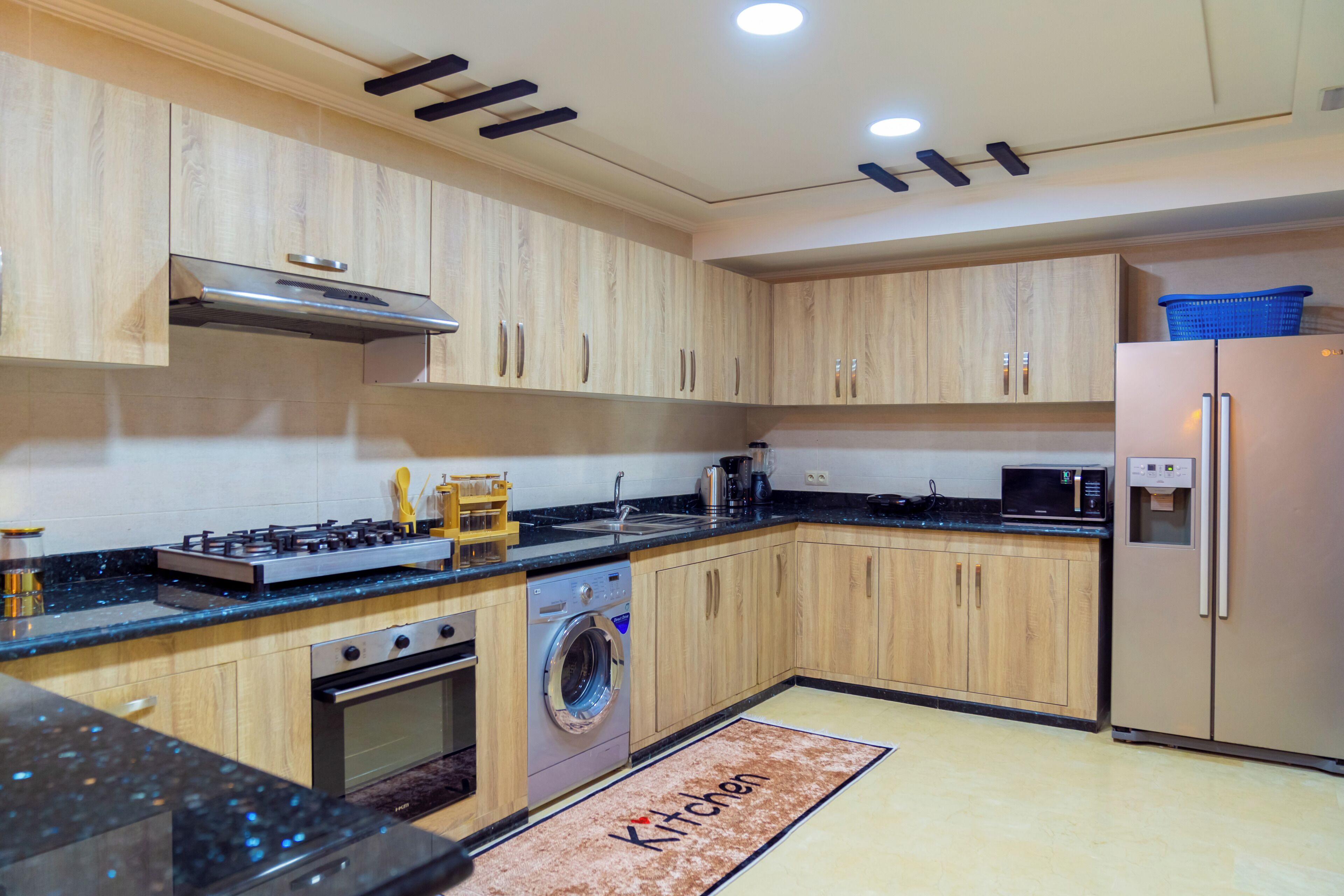 Une cuisine moderne avec des meubles en bois, une cuisinière en acier inoxydable, un lave-linge encastré et un réfrigérateur.