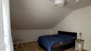 A bedroom with a sloped ceiling, a bed, a chair, a nightstand, and a lamp.
