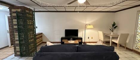 A living room with a ceiling fan, a black sofa, a television, a lamp, and a small table.