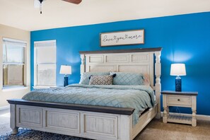Une chambre à coucher comprenant un lit, deux tables de chevet, un ventilateur de plafond, une fenêtre et un mur peint en bleu.