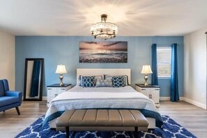 A bedroom with a bed, bedside lamps, a bench, a nightstand, a framed picture, and a window with curtains. - The Mojave Tiki Mirage With Pool - North Las Vegas (North Las Vegas)