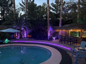 A pool area with a circular pool, lounge chairs, and a thatched-roof structure. - The Mojave Tiki Mirage With Pool - North Las Vegas (North Las Vegas)