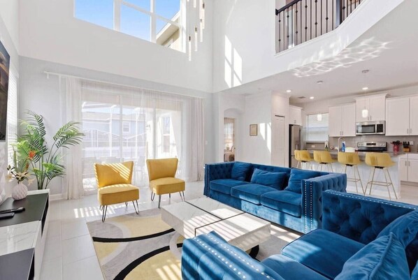 Ein geräumiger Wohnbereich mit einem blauen Sofa, gelben Sesseln und einer Küche im Hintergrund.