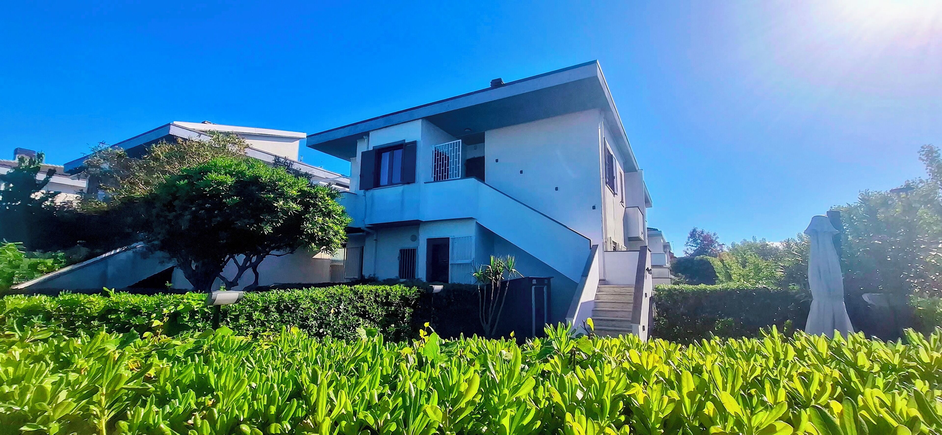 Un edificio moderno a due piani con tetto piatto, una scalinata che conduce all'ingresso e un giardino curato in primo piano.