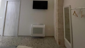 A room with a stone ceiling, a flat-screen TV mounted on the wall, a small air conditioning unit, a bed with a blanket, and a window with a view of the sky. - Casa Corteseapulia, ideale per due persone, immersa nella quiete più totale. (Putignano)
