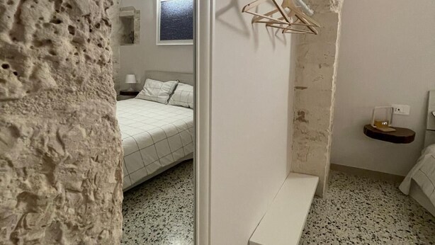 A bedroom with a stone wall, a bed, a hanging light fixture, and a small shelf. - Casa Corteseapulia, ideale per due persone, immersa nella quiete più totale. (Putignano)