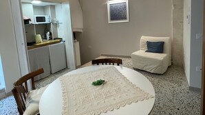 A cozy room with a round table, chairs, a sofa, and a kitchenette in the background. - Casa Corteseapulia, ideale per due persone, immersa nella quiete più totale. (Putignano)