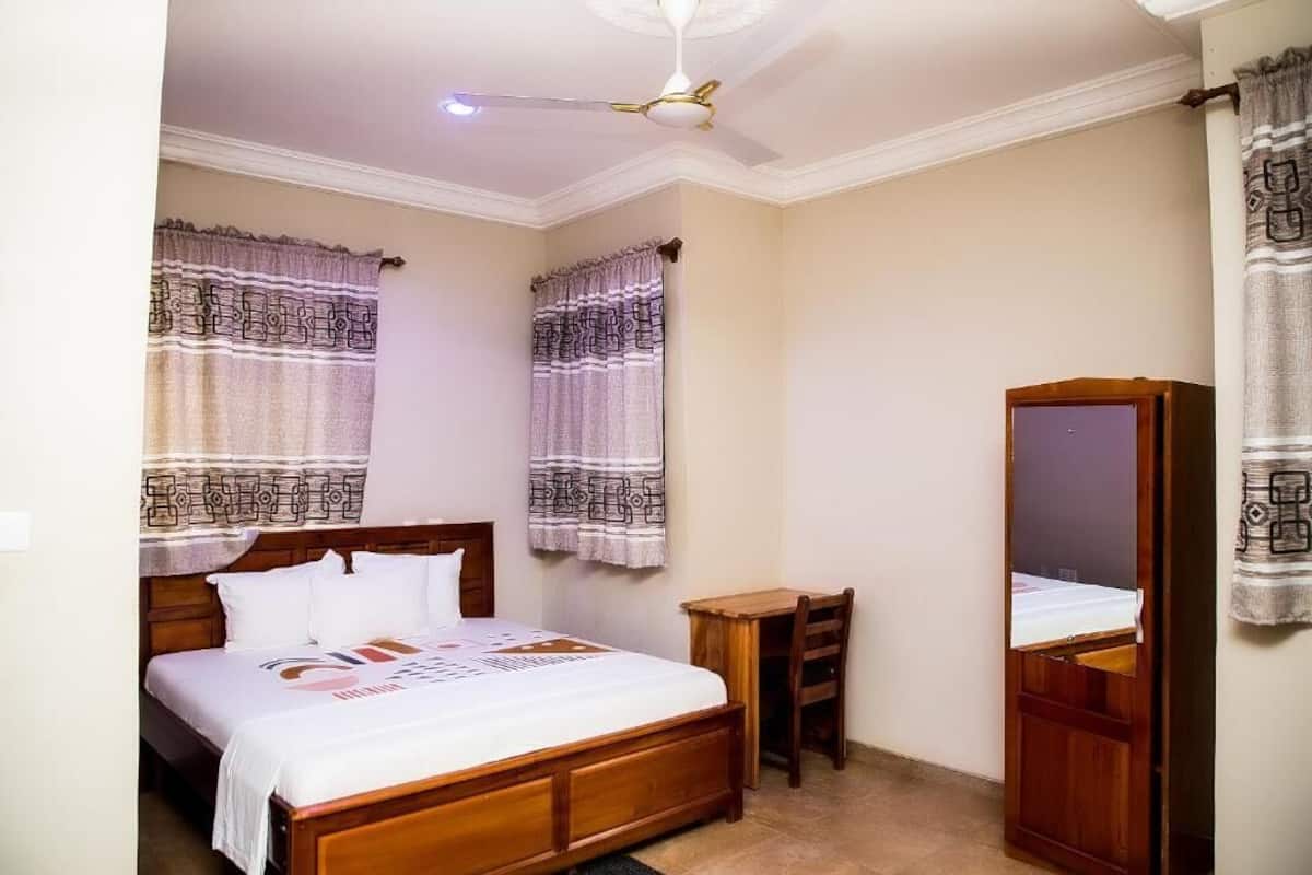 A bedroom with a bed, a desk, a chair, a ceiling fan, and a mirror.