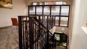 Una escalera con barandillas de metal ornamentadas, piso de piedra y vista al exterior.