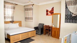 Un dormitorio con cama, escritorio, silla, espejo y ventana con cortinas.