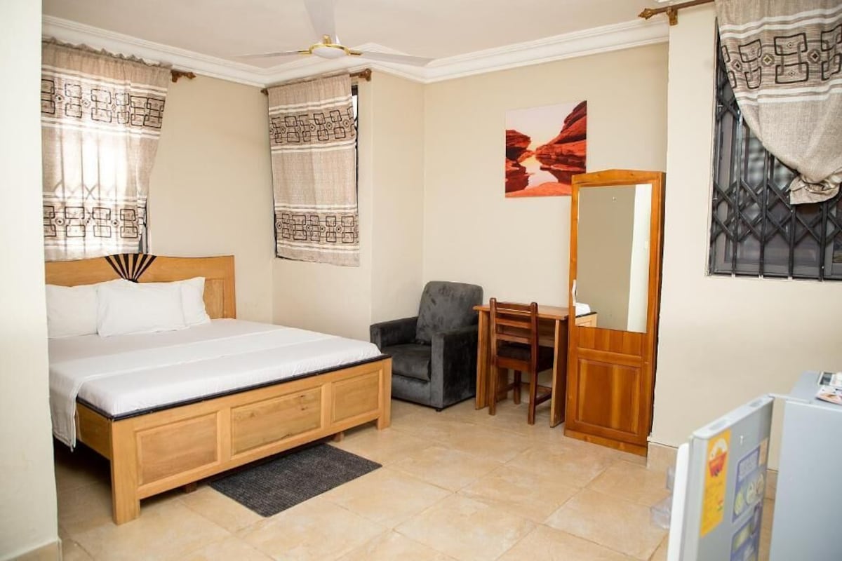A bedroom with a bed, a desk, a chair, a mirror, and a window with curtains.