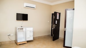 Una habitación con aire acondicionado, televisor de pantalla plana, refrigerador y una puerta con cerradura.