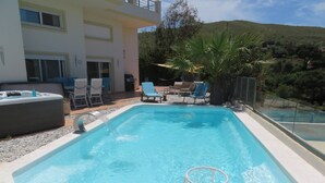 Ein rechteckiger Swimmingpool mit integriertem Basketballkorb, umgeben von Liegestühlen und einem Whirlpool.