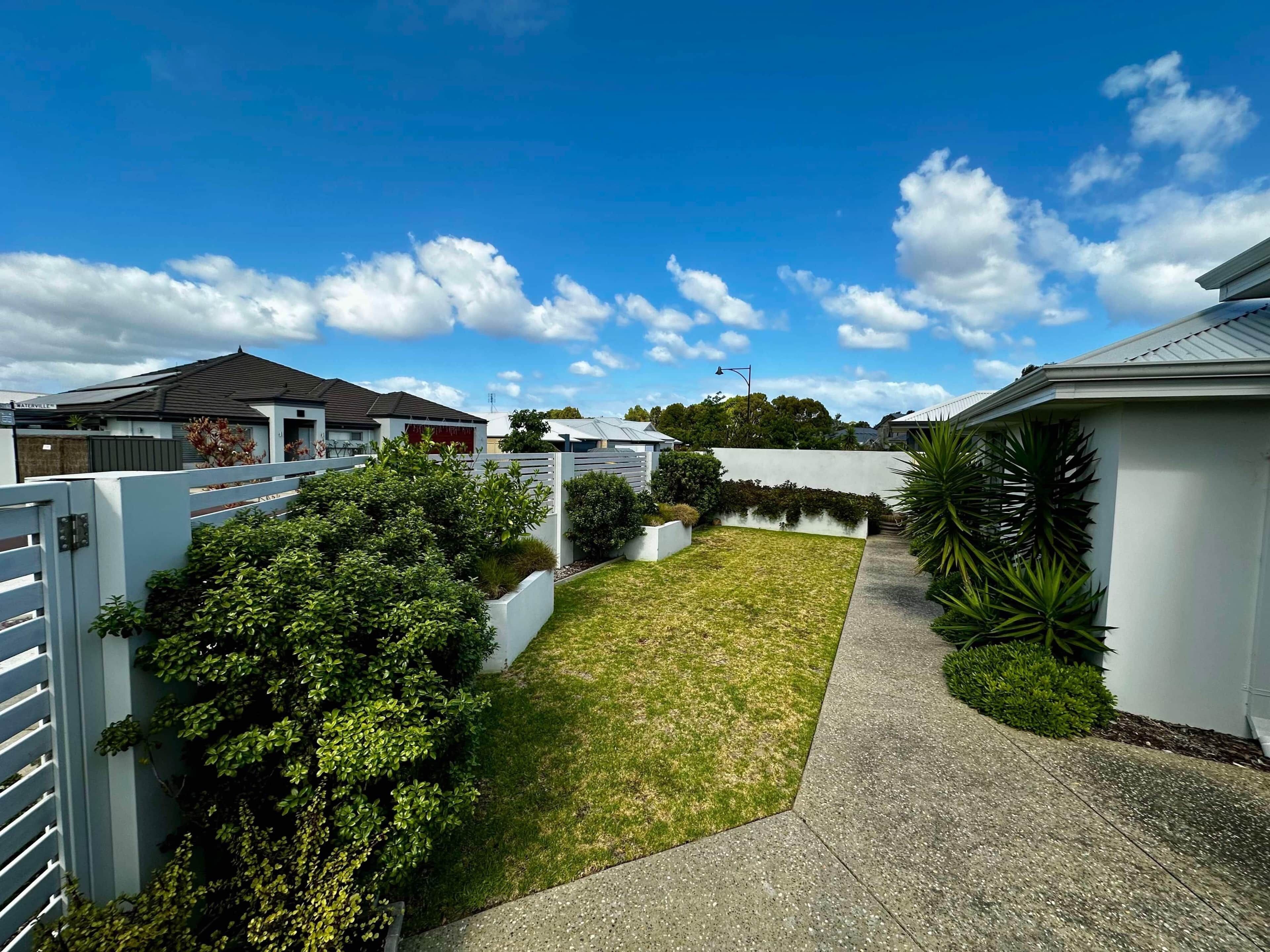 A residential area with houses, a paved pathway, and a grassy lawn.