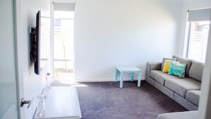 Une pièce avec un canapé gris, une petite table blanche et un tabouret bleu.
