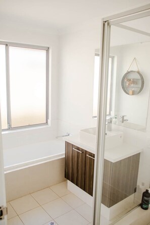 Ein Badezimmer mit Fenster, Waschbecken, Spiegel und Dusche.