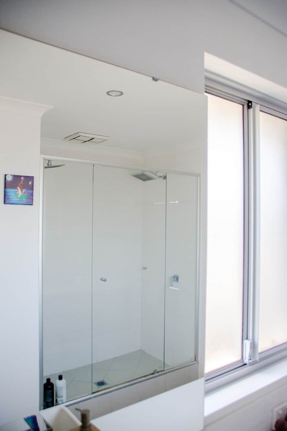 A modern bathroom with a glass shower enclosure, a visible toilet, and a window with blinds.