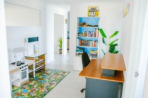 Una habitación con escritorio, estantería y una pequeña zona de cocina con una cocina de juguete.