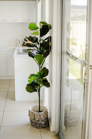 A potted plant in a patterned pot by a sliding glass door in a modern kitchen with white cabinets. - Swell House (Dunsborough)