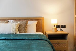 Een bed met een blauwgroene sprei, een houten hoofdbord en een nachtkastje met een lamp.