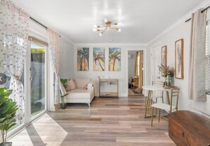 Ein geräumiges Wohnzimmer mit einer Couch, einem Esstisch, Stühlen, einer Chandelüster und Kunstwerken an den Wänden.