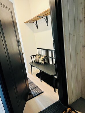 Un couloir avec un banc, une porte et une étagère en bois.