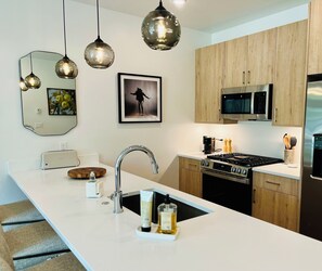 A modern kitchen with a central island, stainless steel appliances, wooden cabinets, pendant lighting, and artwork on the walls. - Silverthorne Retreat with Mtn Views, Private Saltwater Hot Tub, King Bed & Bidet (Silverthorne)