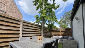 Un patio con una mesa y sillas, una cerca de madera y un árbol.
