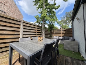 Eine Terrasse mit Tisch und Stühlen, einem Holzzaun und einem Baum.