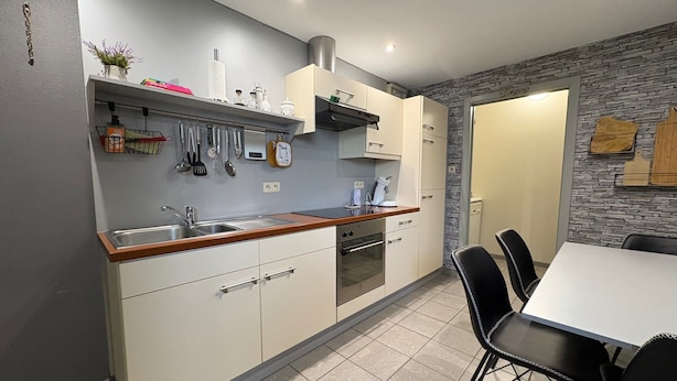 Una cocina moderna con horno integrado, un lavabo y una zona de comedor con mesa y sillas.