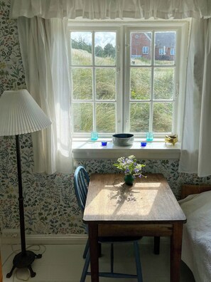 Ein Zimmer mit Fenster, einem Tisch mit Vase, einer Lampe und strukturierten Tapeten.