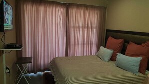 A hotel room with a bed, curtains, a TV, and a small table. - Room-boutique Self Catering Guesthouse 4 (Johannesburg)