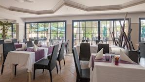 Un restaurante con mesas dispuestas para comer, sillas y grandes ventanales que ofrecen vistas al exterior.