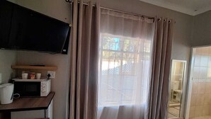 Een slaapkamer met een bed, een aan de muur bevestigde televisie, een bureau met een magnetron en een raam met gordijnen.