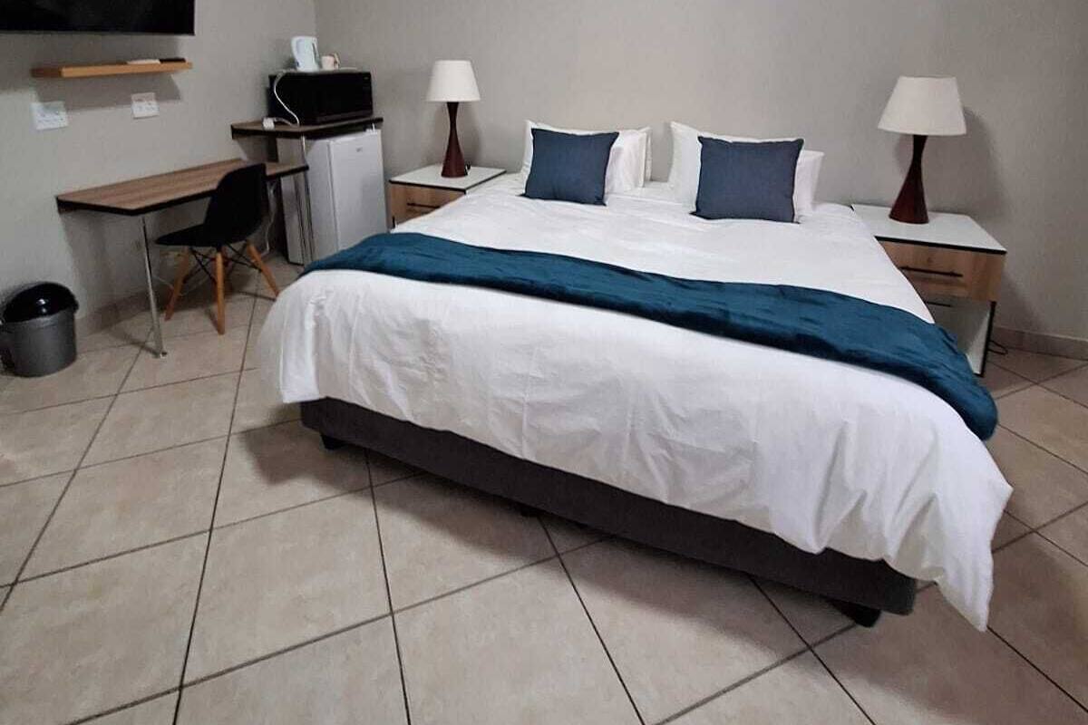 A hotel room with a bed, a desk, a chair, a TV, and two bedside lamps.