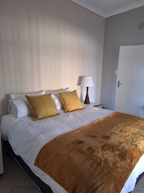 A hotel room with a bed, pillows, a lamp, and a door. - Rams Blissful Guest House (Rustenburg)